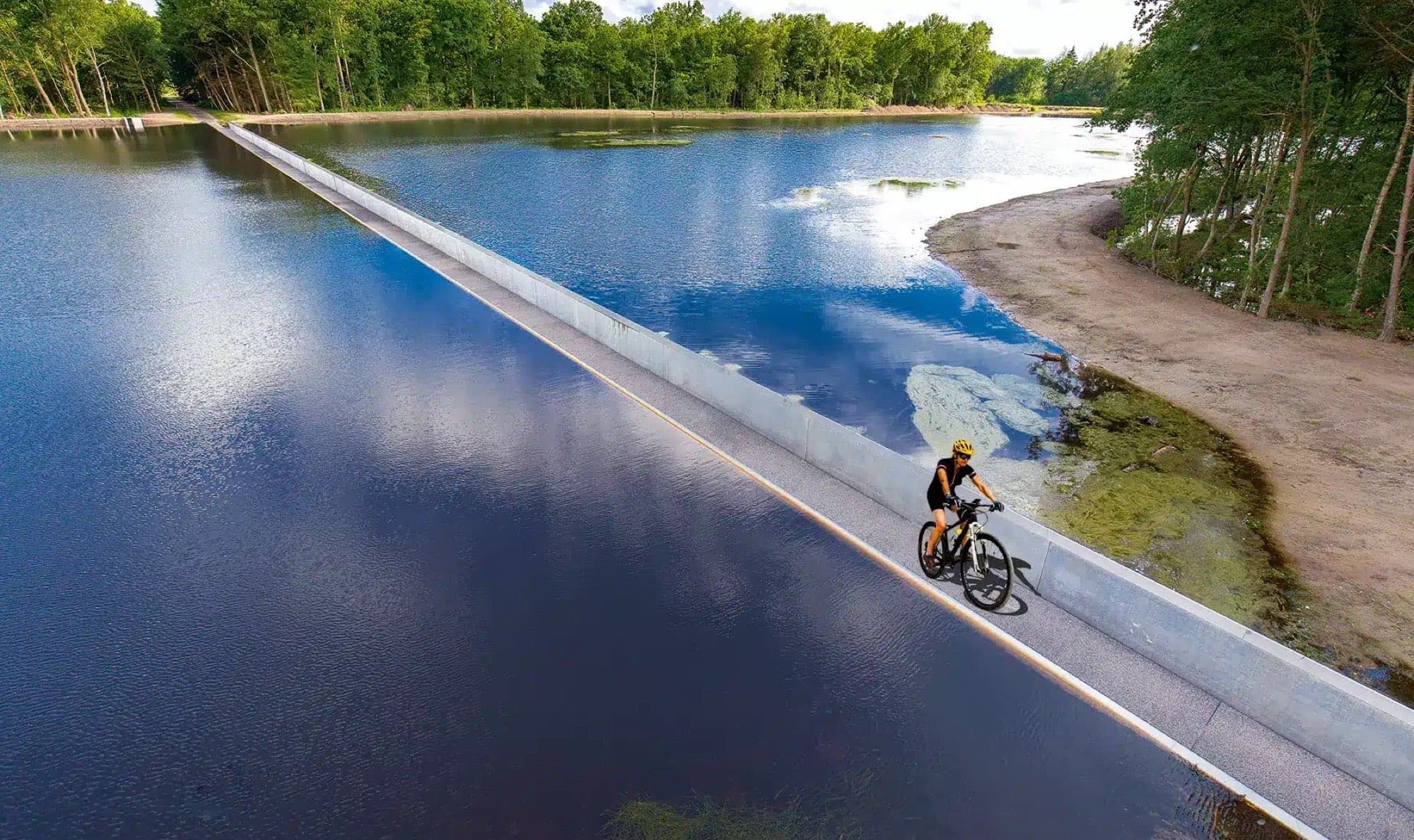 Cyclist in the sunken concrete path at eye level with the pond, Bokrijk